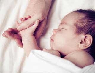 Parent holding a sleeping newborn baby's hand