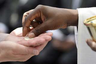 Close-up of a priest's hands as he places the Host in the palm of a parishioner