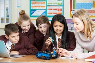 Four school children and their teacher working on building a robot in the classroom