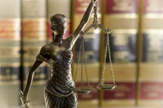 A statue of Lady Justice stands in front of a row of legal books