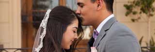 A loving husband kisses his smiling wife's forehead on their wedding day