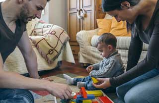 A young boy and his parents play with building blocks on their living room floor
