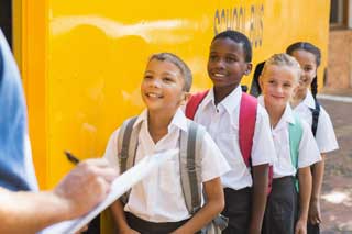 A group of smiling school children standing in line to board a school bus