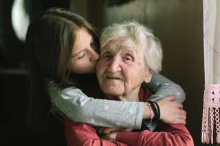 A young girl kissing a smiling elderly woman on the cheek