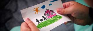 A young child's hands holding a drawing of a house and family