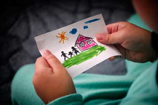 A young child's hands holding a drawing of a house and family