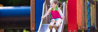 A young girl gets ready to go down a slide at the park