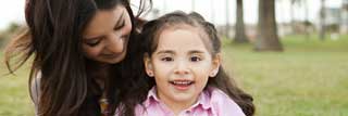 A mother holds her smiling daughter in a public park