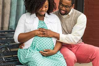 An expectant mother and her husband smile while they both touch her belly