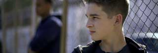 Two incarcerated young men lean against a chain link fence, staring into the distance