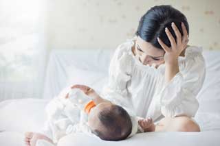 An overwhelmed mother bottle-feeding her newborn baby