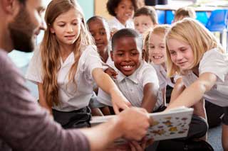 A teacher reads a story to a group of school children in uniform