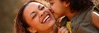 A smiling mother being kissed on the cheek by her young daughter