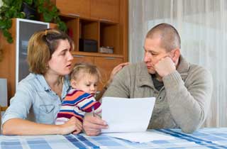 A young mother and father hold their small daughter while figuring out their financial situation