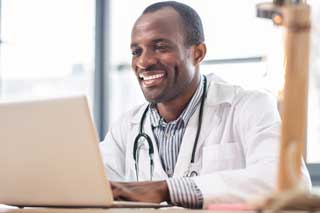 A smiling doctor reviews patient records on his computer