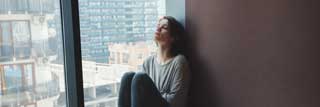 A depressed woman sitting against the wall in her apartment