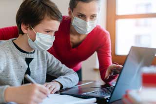 A student and teacher wearing masks, working together to solve a problem on a laptop