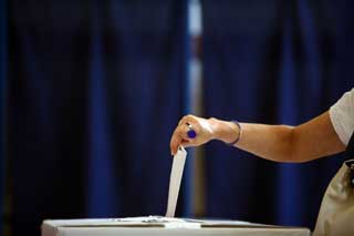 A woman's hand inserting her ballot into a ballot box