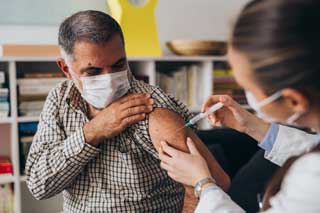 A man wearing a protective facemask receiving a vaccination shot from his doctor