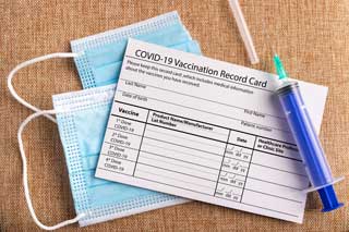 Conceptual image of a COVID-19 vaccination record card, disposable face mask, and hypodermic needle.