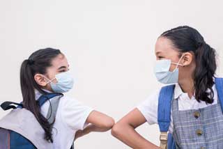 Two school girls wearing protective face masks bump elbows