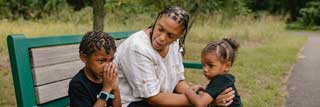 A mother and her two children sitting on a park bench.