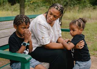 A mother and her two children sitting on a park bench.