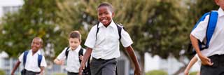 Five smiling children wearing school uniforms running in the grass