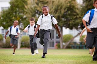Five smiling children wearing school uniforms running in the grass