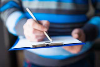 Closeup of a man signing a petition attached to a clipboard