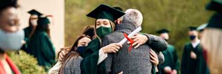 A smiling student embracing her family, surrounded by other students and families on her graduation day during the COVID-19 pandemic.