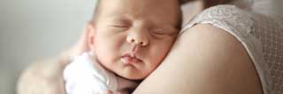 A mother holding her sleeping, newborn child.