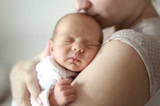 A mother holding her sleeping, newborn child.