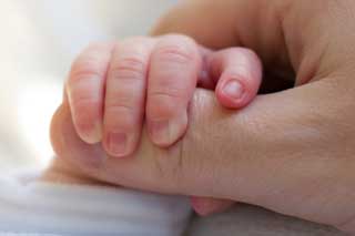 Closeup of a newborn baby’s hand grasping their parent’s thumb
