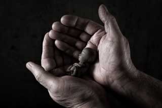 Black and white photo of cupped hands holding a depiction of a fetus