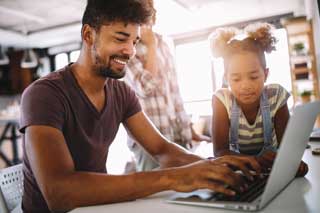 A smiling father and daughter working together on a laptop