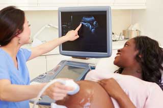 A nurse pointing to an ultrasound image of a pregnant woman's child.