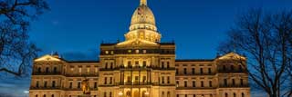 The exterior of the Michigan State Capitol building, lit up at dusk.