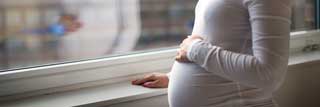 A young pregnant woman staring out of her apartment window.