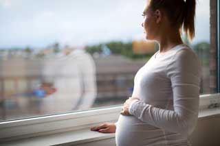 A young pregnant woman staring out of her apartment window.