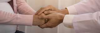 A pregnant woman clasping hands with another person who is comforting them.