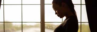 A young pregnant woman outlined by the light coming in from the window behind her.