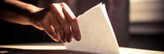 A hand reaching out and placing a folded ballot into a ballot box