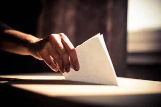 A hand reaching out and placing a folded ballot into a ballot box