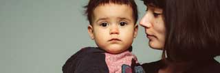 A young woman holding and looking at her child who is in turn looking at the camera.