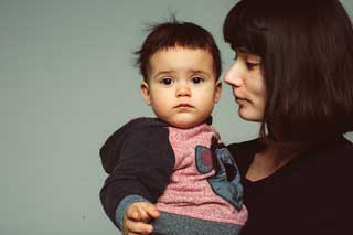 A young woman holding and looking at her child who is in turn looking at the camera.
