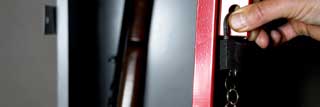A hand preparing to close the door on a gun safe, thus locking a rifle inside.