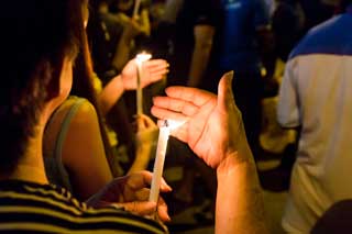 Closeup of a woman's hands shielding a lit candle during a candlelight vigil.
