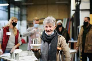 A smiling, older woman holding a bowl of soup in a soup kitchen.