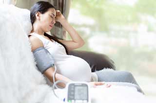 A young, pregnant woman sitting on her sofa, looking concerned.